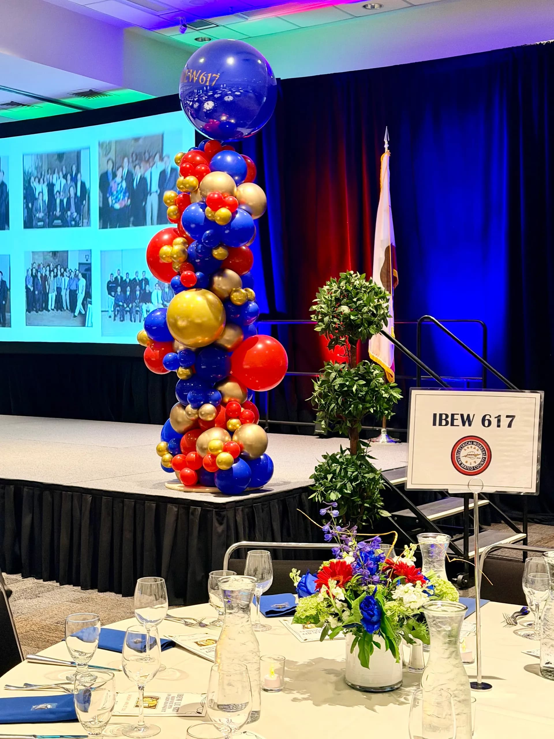 Corporate event décor by Balloon Décor: branded balloon backdrop and stage columns in red, royal blue and gold, San Mateo, California — view 6.